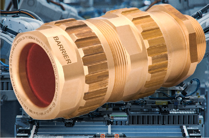 Large brass cylindrical mechanical part labeled 'BARRIER' being moved by industrial machinery in a factory setting.